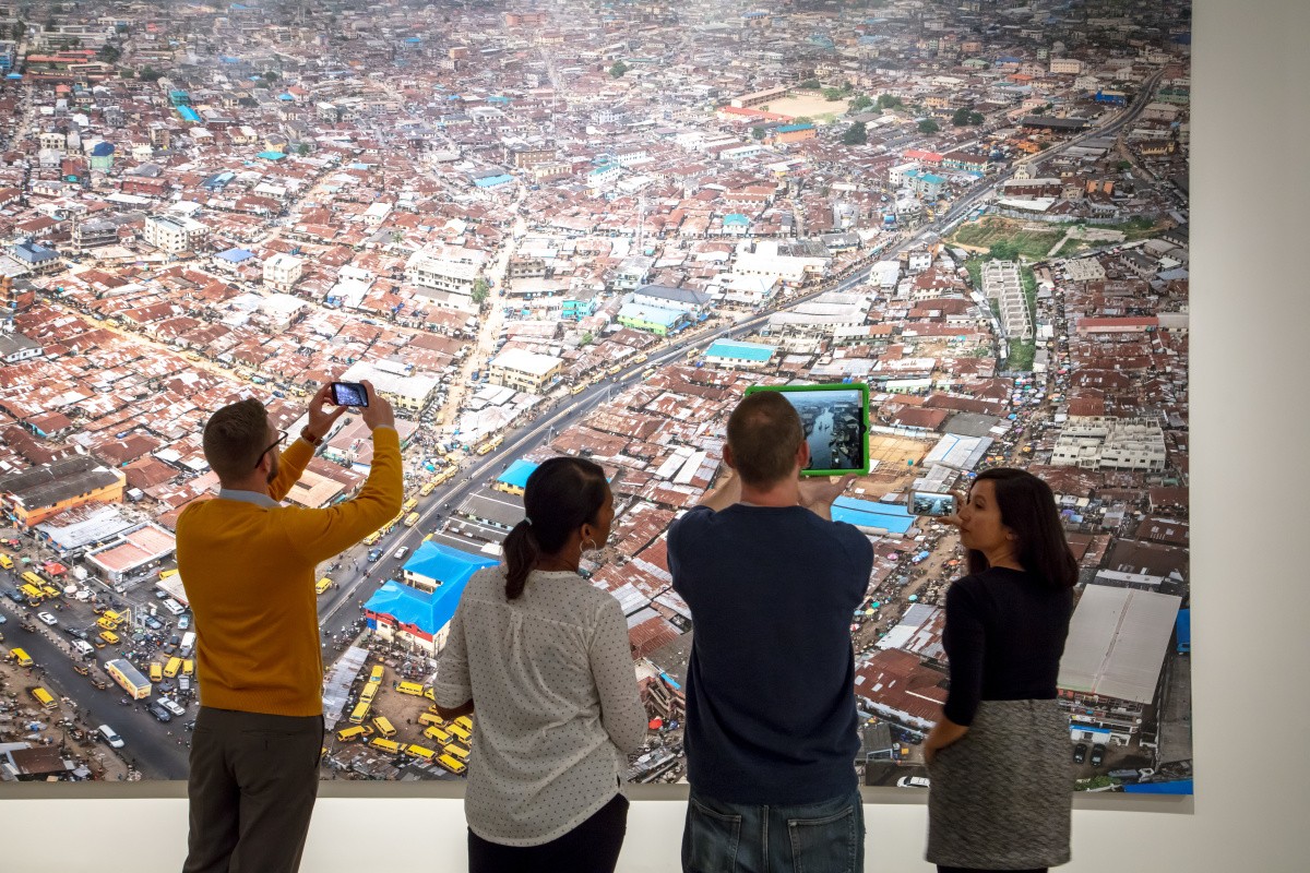 Four individuals stand in front of a mural depicting an aerial view of a city.  