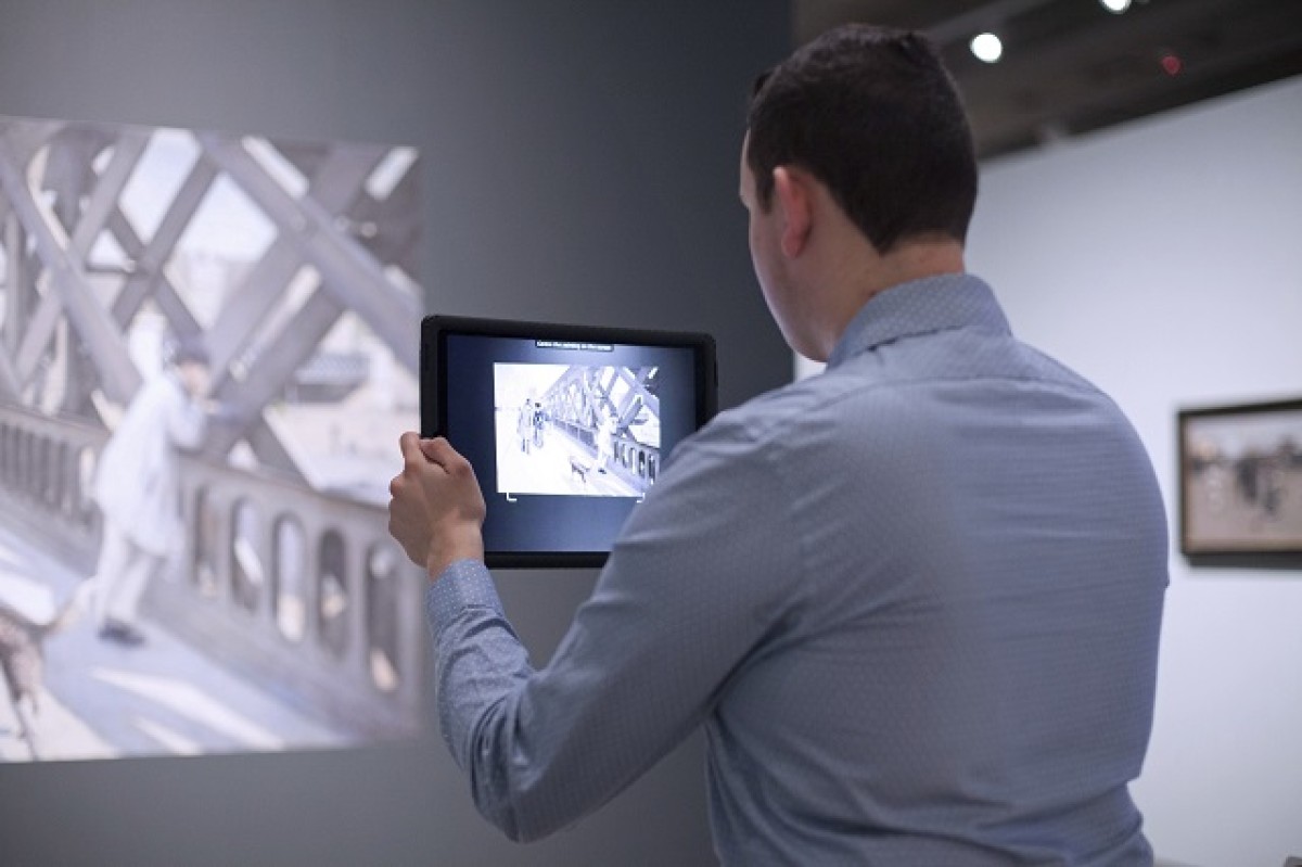 A visitor using AR to view Impressionism in the Age of Industry, 2019. Work shown: Gustave Caillebotte. Le Pont de l’Europe, 1876. Association des Amis du Petit Palais, Genève.