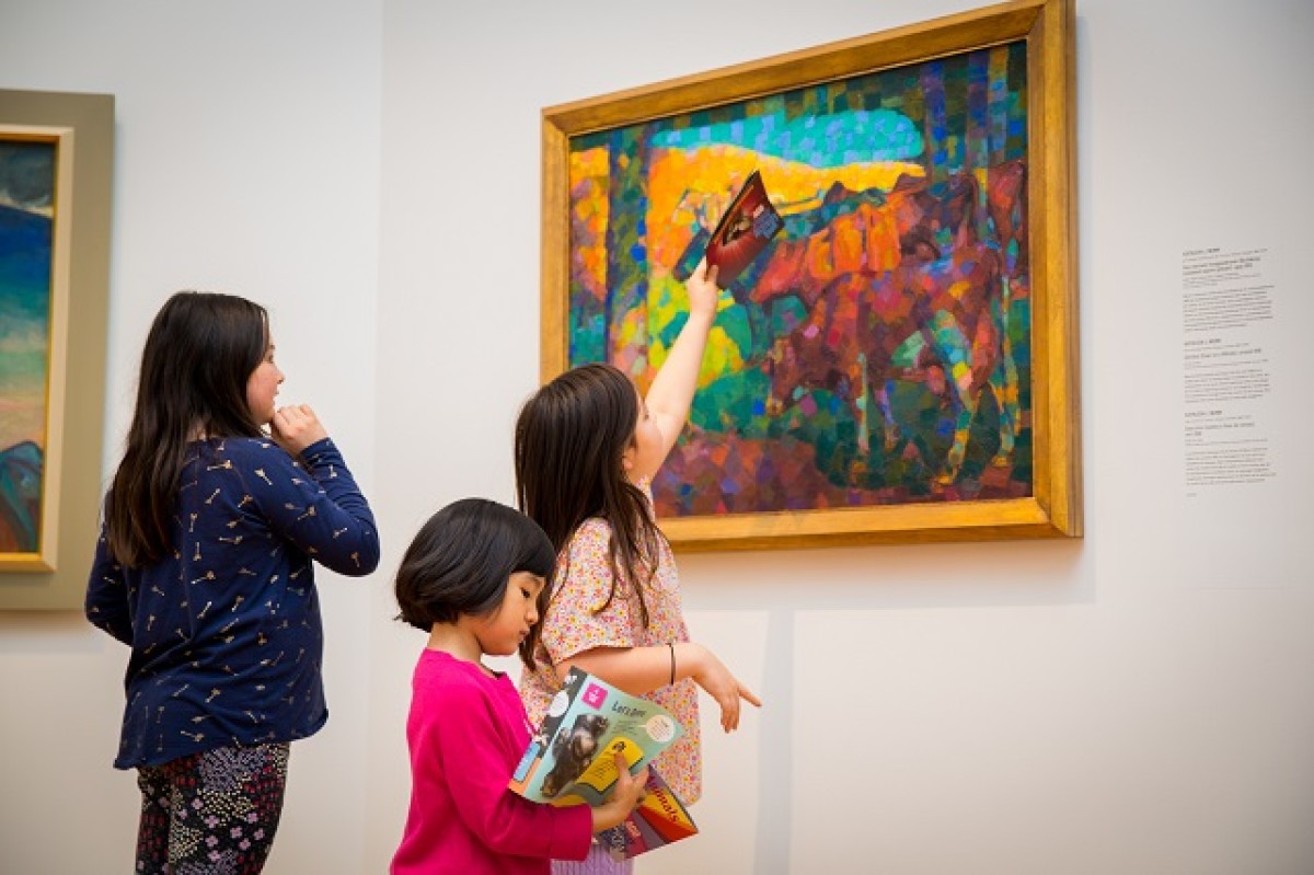 Three young girls looking closely at a Kathleen Munn painting.