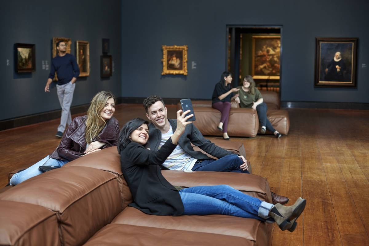 Group of young adults in the gallery looking at a mobile phone.