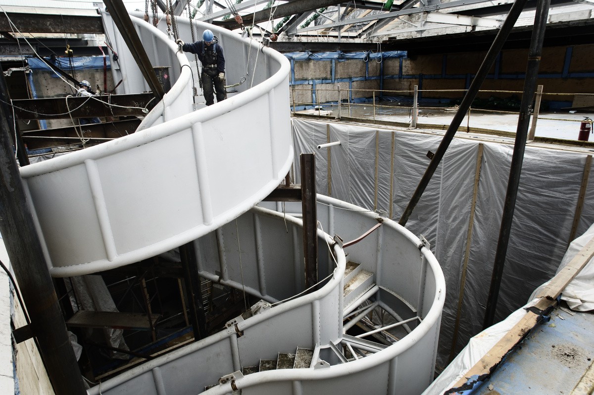 the exposed steel of a spiral staircase under construction is visible with workers