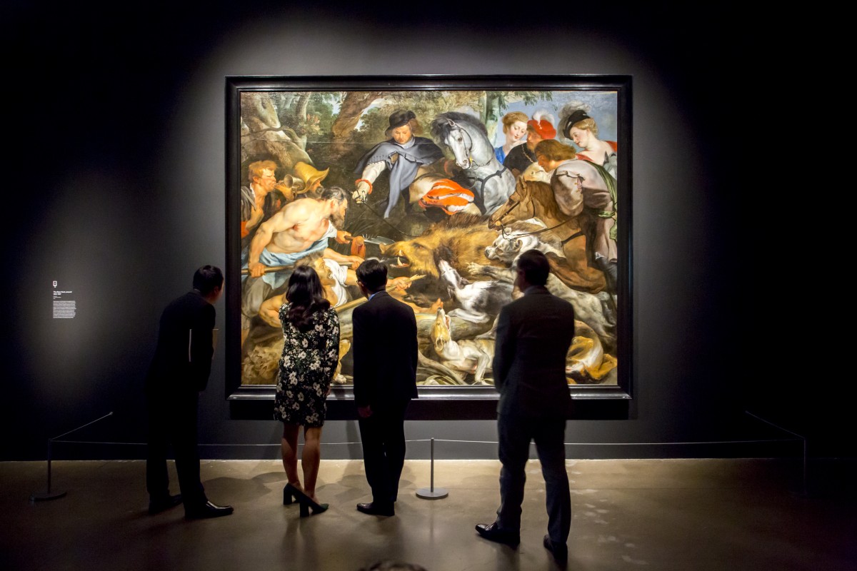 People looking at a large painting by Rubens called the Boar Hunt.