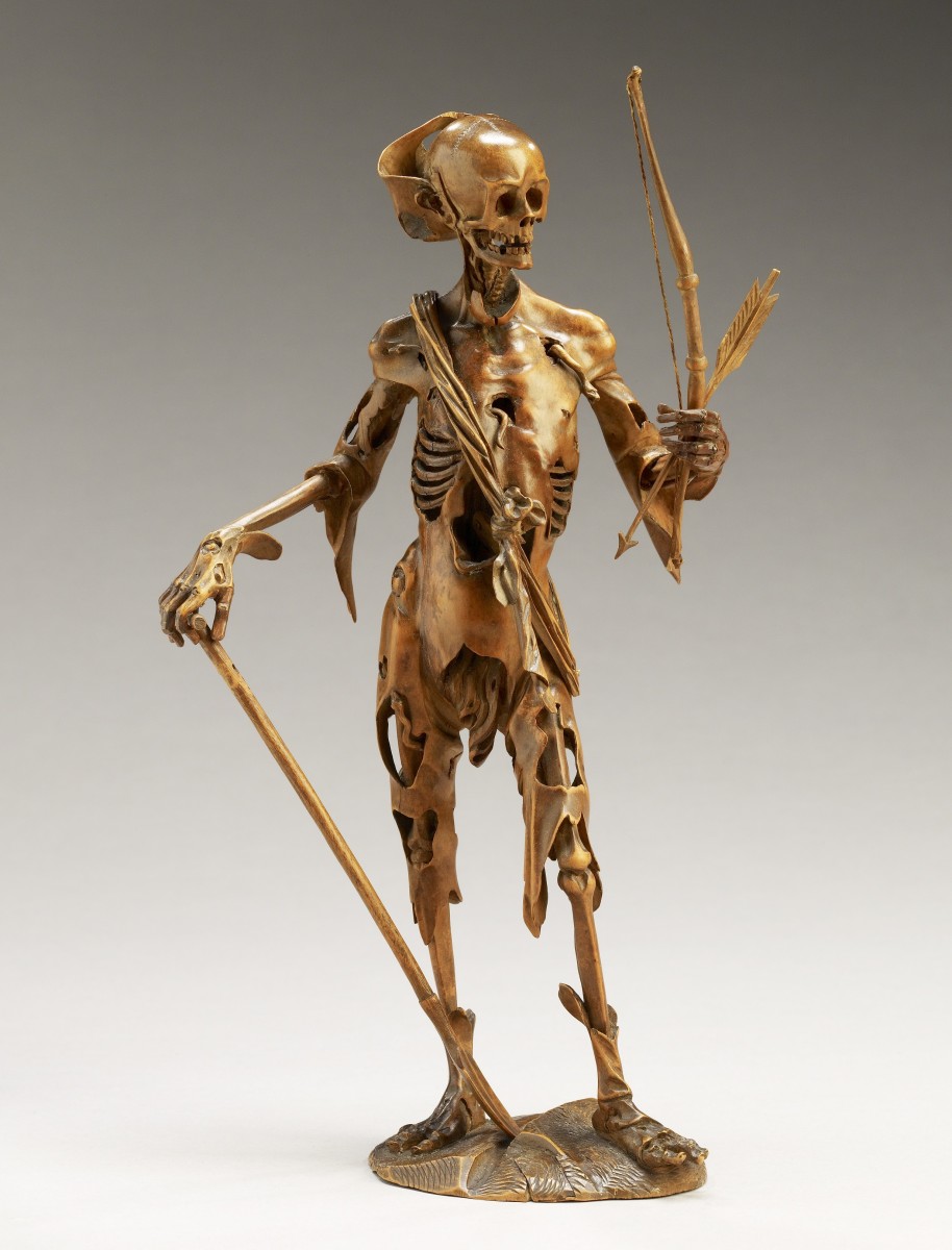 A wooden carving of a skeleton holding a shovel and a bow and arrow.