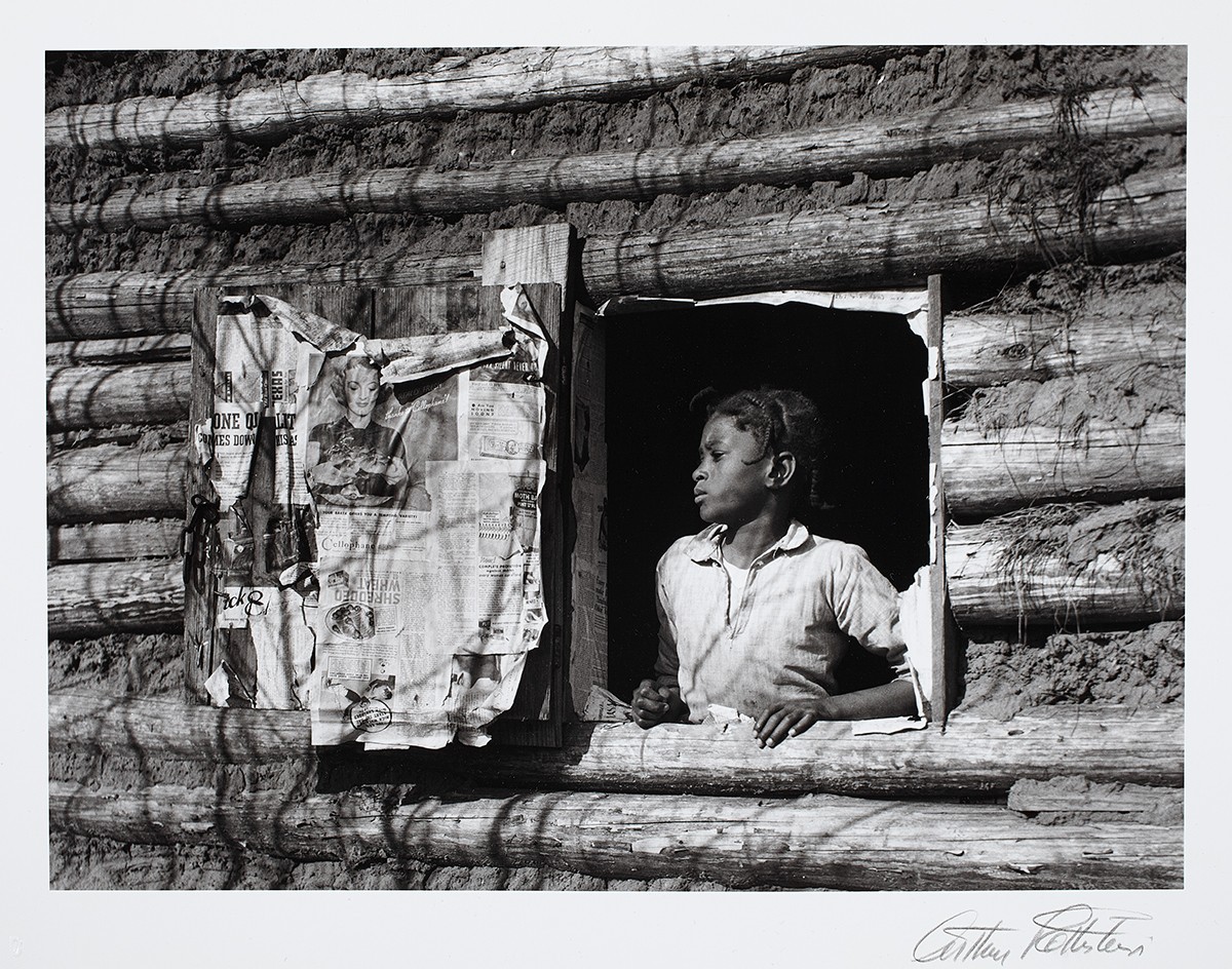 Gelatin silver print of young person looking out log cabin window