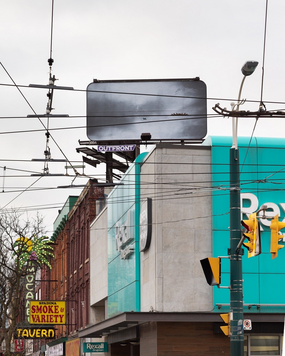 Photo of a Black and white billboard, perched over intersection of Spadina and College street. 