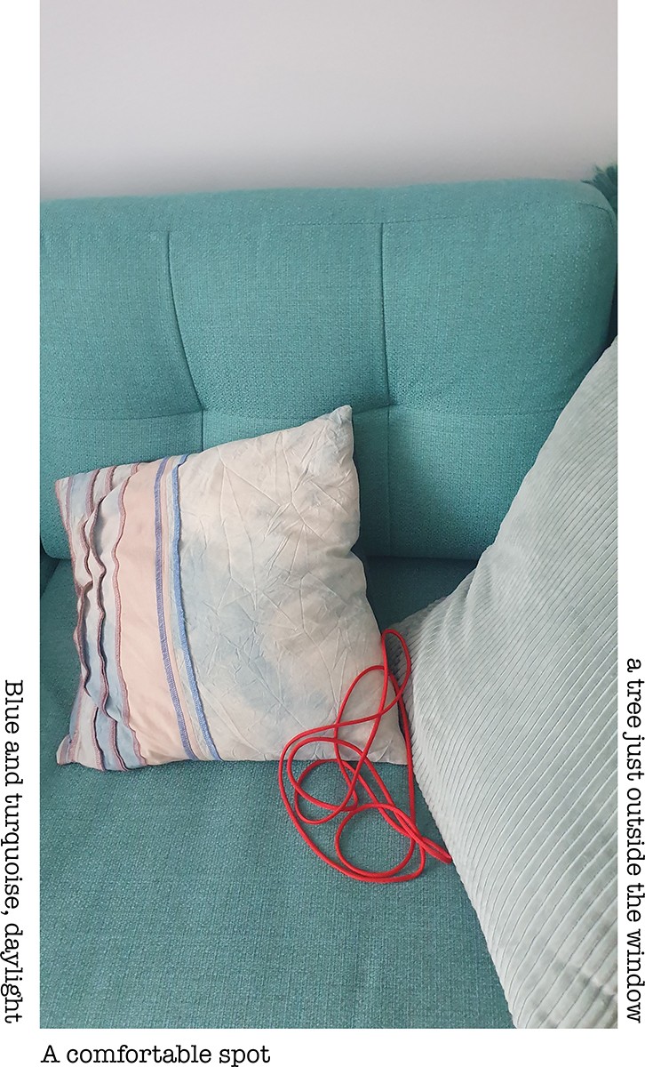 A photo of a red string placed on a blue and turquoise couch with two couch cushions. One cushion on the right side of the photo is smaller than the other one on the left side, cropped by the frame. The small cushion has stripes in different, pastel tones of colours. The big one is made of pale green corduroy. The red string made in a loop is placed between of the two cushions. The following words are displayed: Blue and turquoise, daylight. A comfortable spot. A free just outside the window.