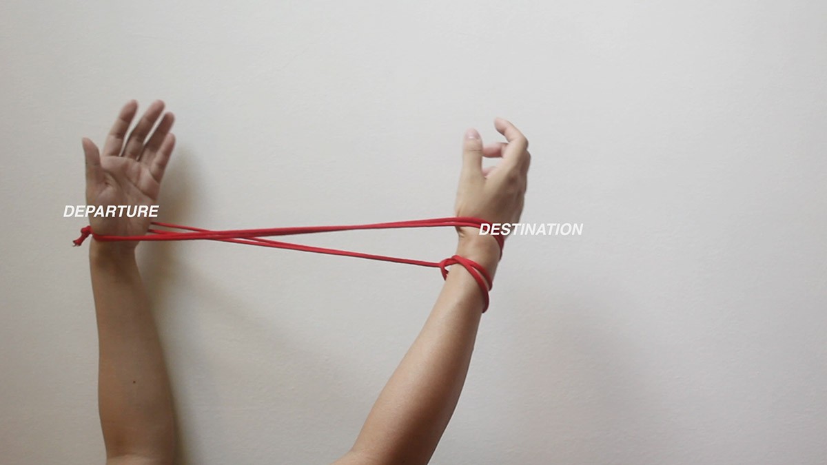 A still cut of a video where two hands are being tied by a loose string loop. On the left palm, it reads: departure, and on the other palm, it reads: destination.