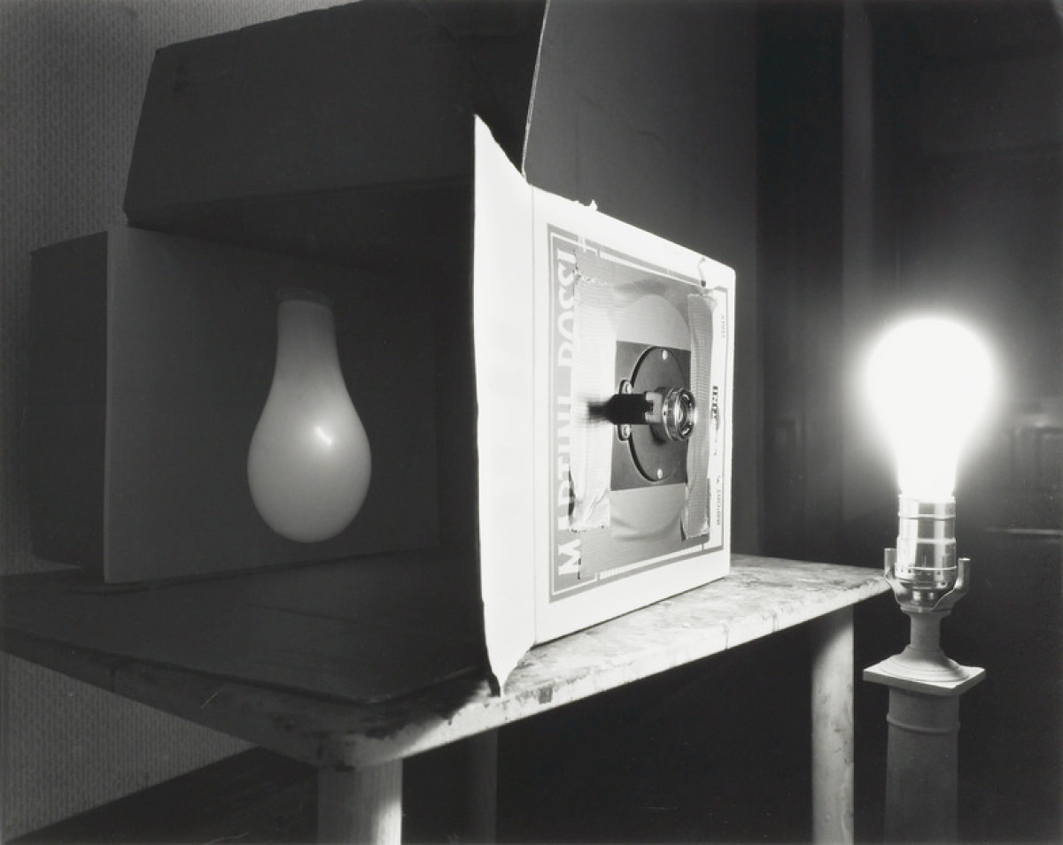 Black and white image of a pinhole camera, lightbulb illuminated