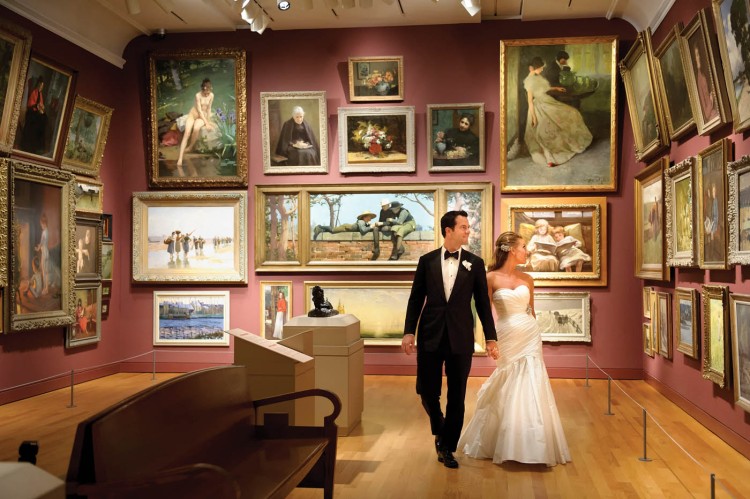 bride and groom holding hands and looking at paintings in gallery