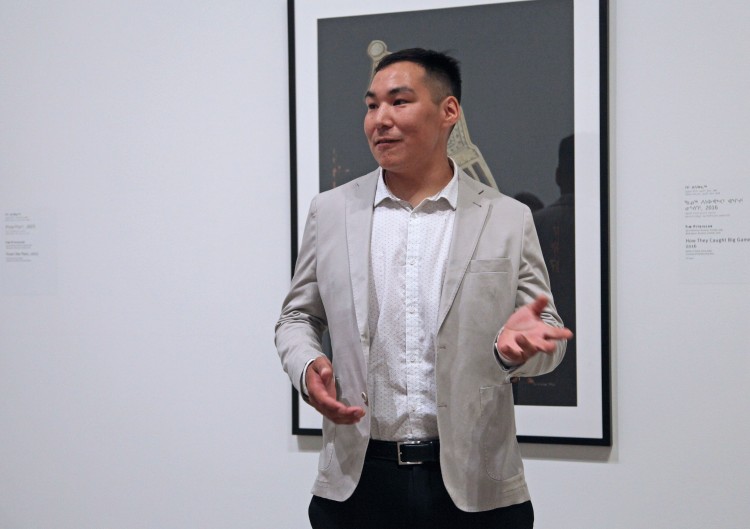 Tunirrusiangit co-curator Koomutauk Curley in front of a Tim Pitsiulak work