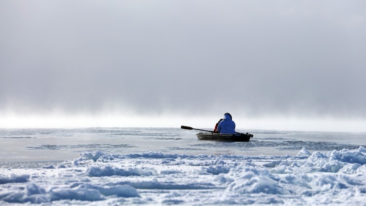 A person rows a canoe in icy water.