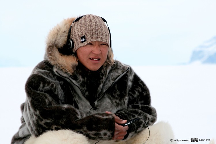 An Inuit teenager wears headphones over a beige tuque and a fur coat.