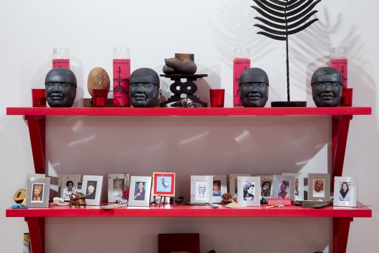 A number of photographs and sculptures sit on red shelves with candles.