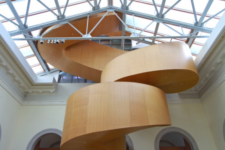 View of a wooden spiral staircase reaching up and going through a glass ceiling.