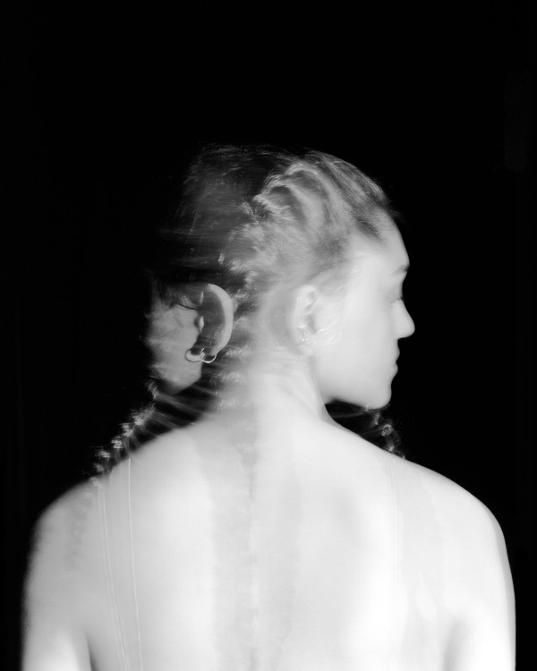 A black and white photograph of a woman, taken from behind as she looks over her right shoulder.