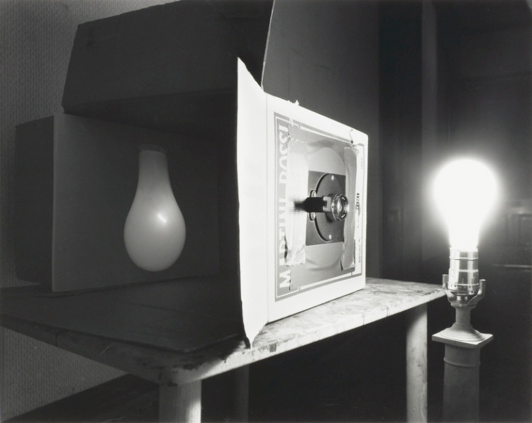 Black and white image of a pinhole camera, lightbulb illuminated