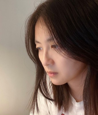 Mingyan looks away from the camera. They are pictured with long brown hair and a white shirt.