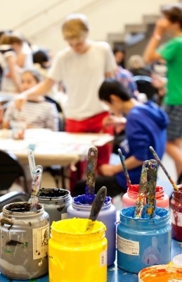 paint and brushes in foreground of students at tables in art class