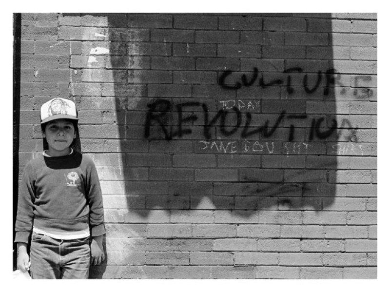 a boy standing near a brick wall with graffiti