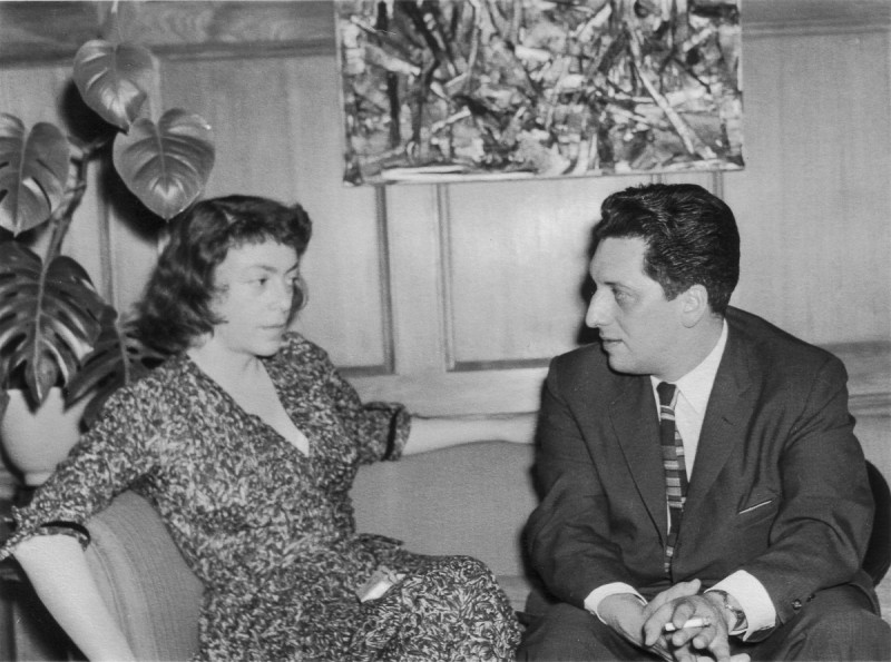 image of artists Joan MItchel and Jean-Paul Riopelle seated on a sofa in front of Riopelle's paintings