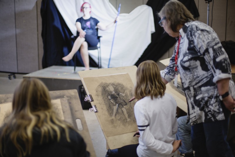 instructor with student in life drawing class, model in background