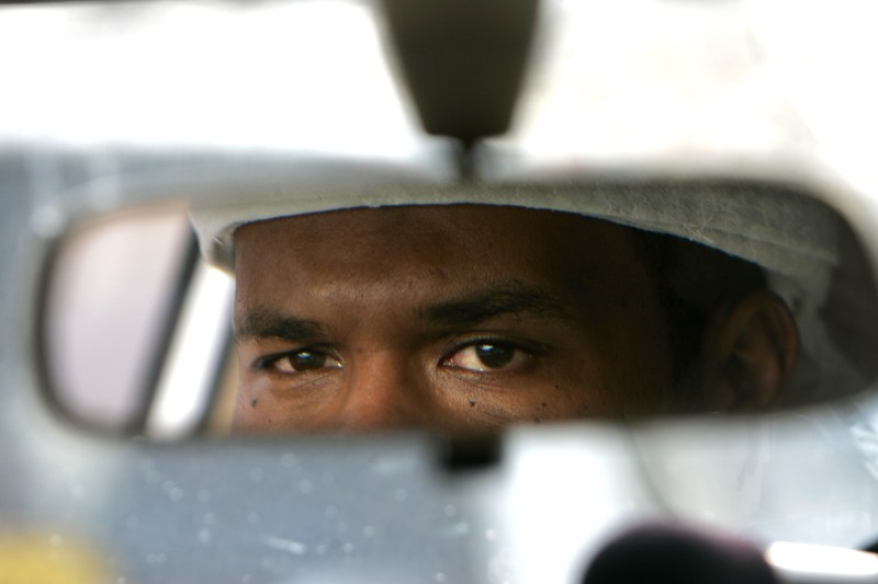 Film still from The Oath, a mans eyes visible in a rear-view car mirror