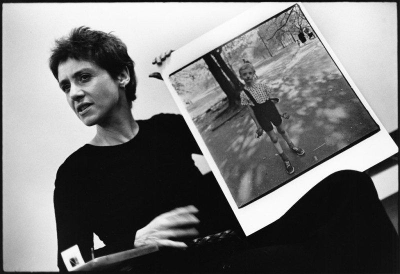 Photographer Diane Arbus in black holding a print of her photo while discussing her work in a presentation 