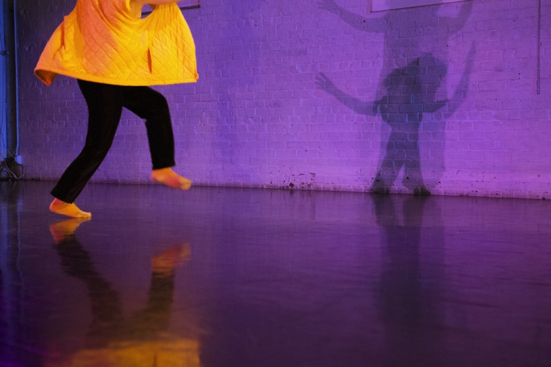 Person in yellow coat casts shadow on purple wall. 