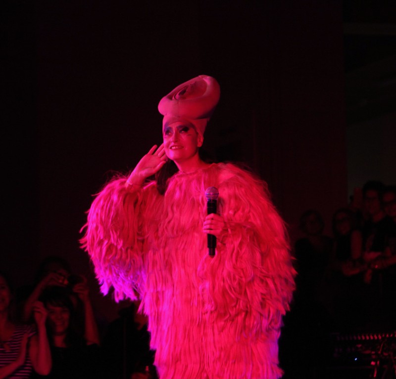 Figure in furry pink costume against black background. 