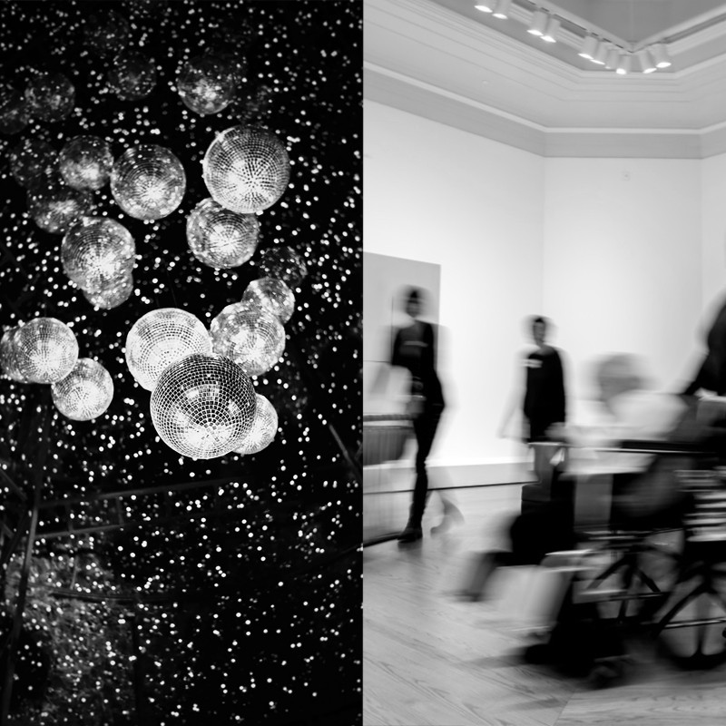(Left) Disco balls hang from the celling surrounded by sparkling lights. (Right) A individual in a wheel chair and two individual standing upright pass across the frame. They are blurred, out of focus.