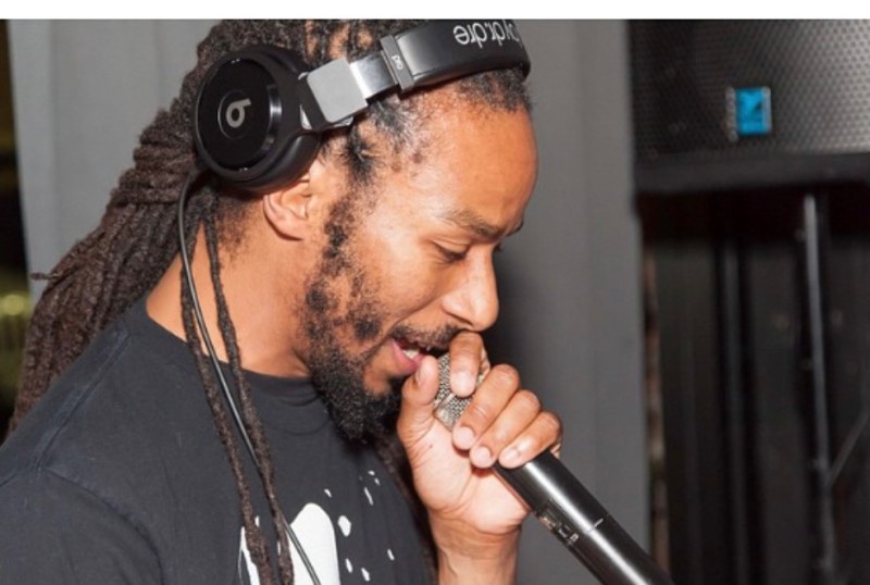 photo of DJ Kevin Hood in profile, wearing black beatz headphones, black tshirt, speaking into a mic