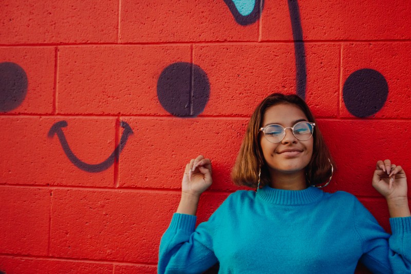 Vanessa Figuero infront of a red brick wall spray painted with a smiley face