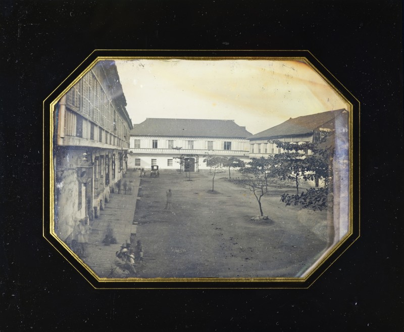 Black border around a sepia toned photograph of buildings surrounding a pavilion