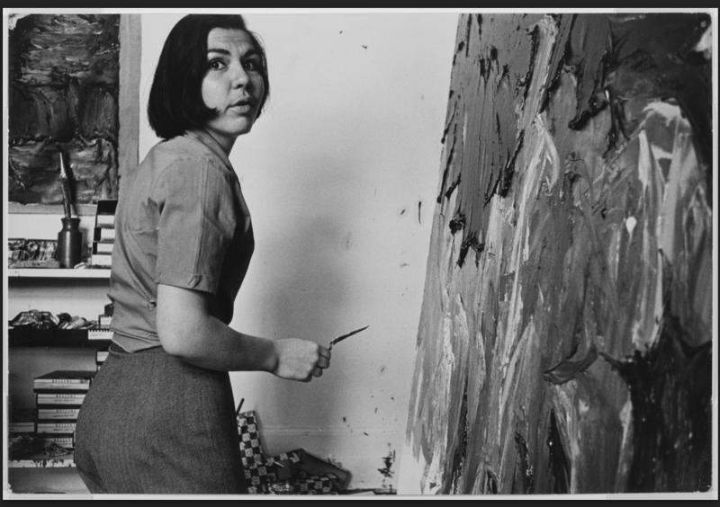 Black and white photo of artist Letendre in her studio in front of a painting in progress. 