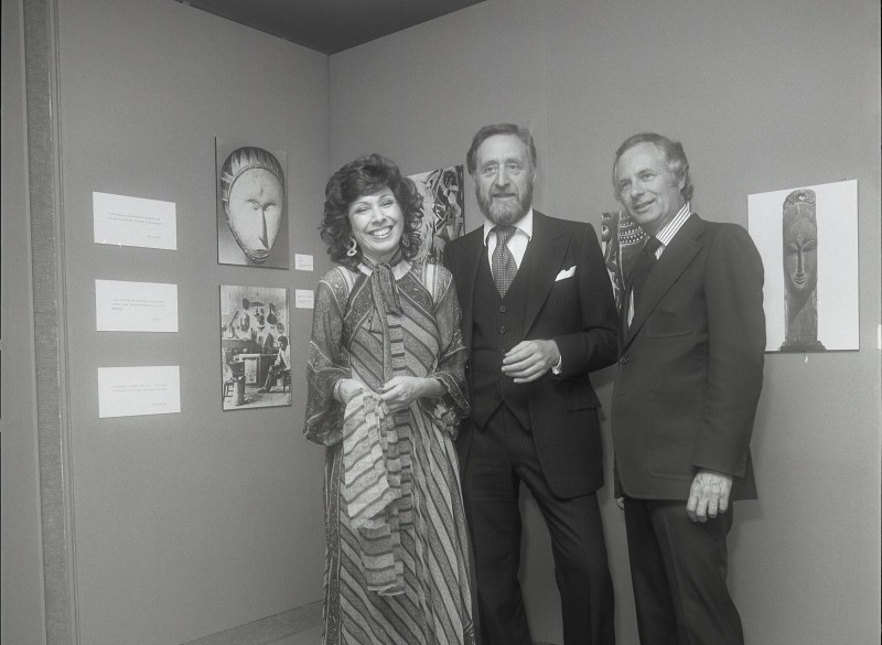 Black and white photograph of three people standing together and smiling. 