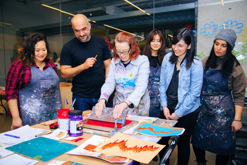 And instructor conducts screen printing with red paint, while students stand behind and observe