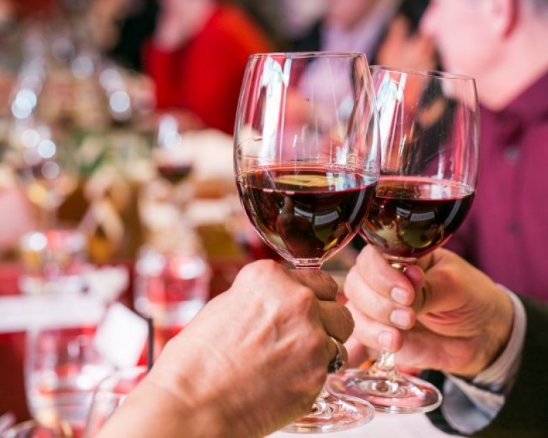 Two glasses of red wine at a dinner event, they are in a cheers gesture where the glasses are meeting. 