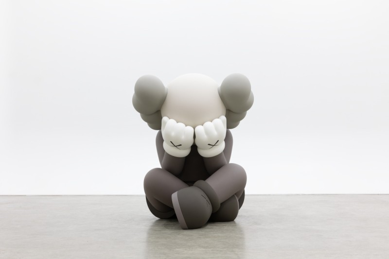 photo of KAWS sculpture Separated, featuring Companion sitting cross legged, hands covering their eyes. Sculpture is bronze and painted in shades of gray