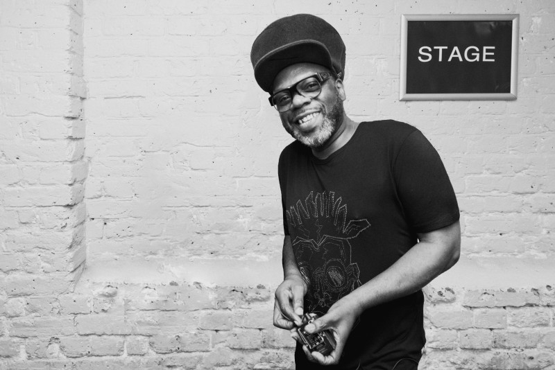 Jazzie B in a black and white photo under a stage sign. 