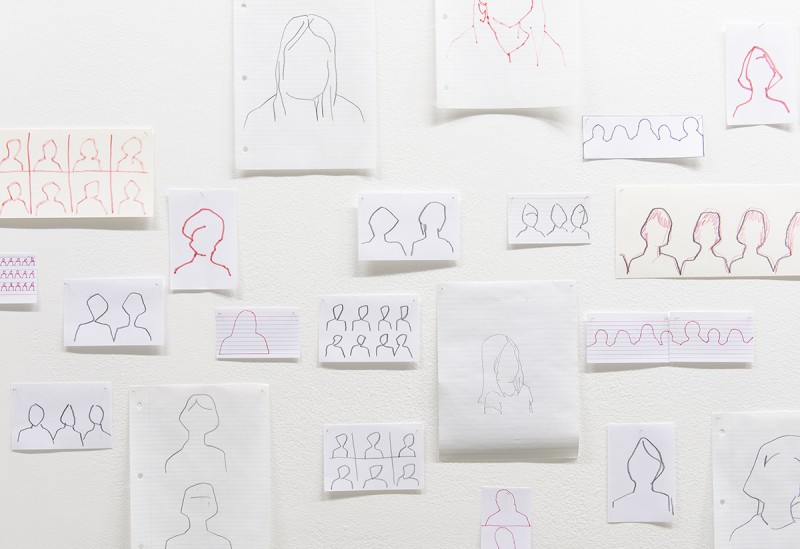 Installation view of figure drawings taped to wall