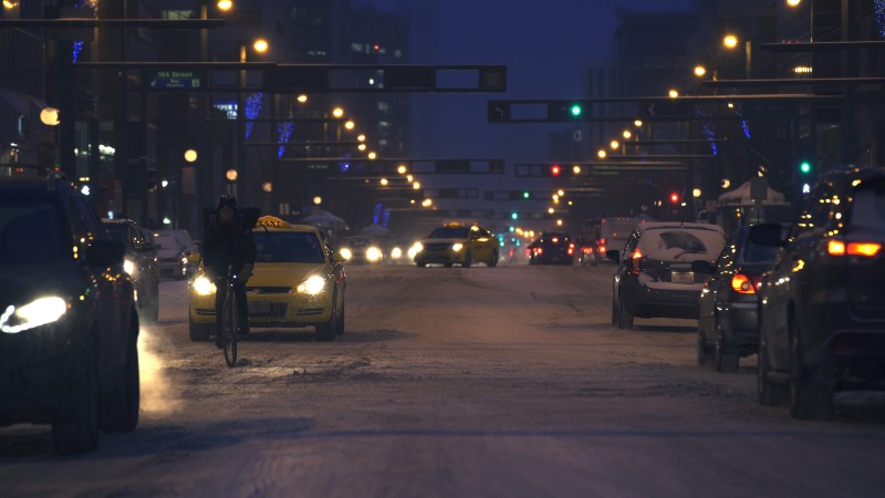 Still image of Edmonton at night in the snow with a single cyclist with cars