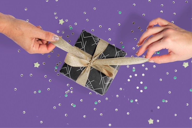 two hands tying on bow on a gift box with a stylized background