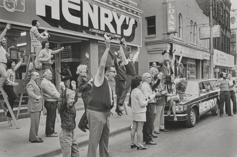 Black and white photograph of a group of people celebrating in 1974 in front of the Henry's location on Church Street in Toronto.