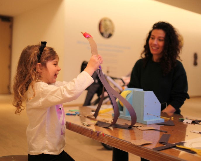 Child and adult in the Community Gallery. The child is holding a paper animal.